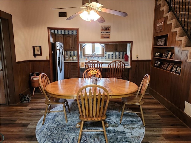 dining room featuring wooden walls, ceiling fan, dark wood-style floors, and a wainscoted wall