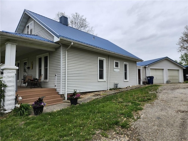view of property exterior featuring covered porch, metal roof, a chimney, an outbuilding, and a detached garage