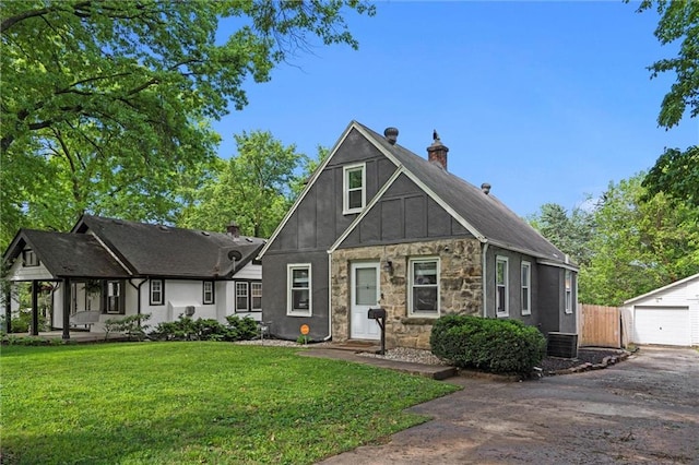 8242 Belleview Ave, Kansas City, MO 64114 - tudor-style house with board and batten siding, an outdoor structure, a chimney, asphalt driveway, and stone siding