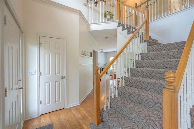 stairs with baseboards, a ceiling fan, a towering ceiling, and wood finished floors