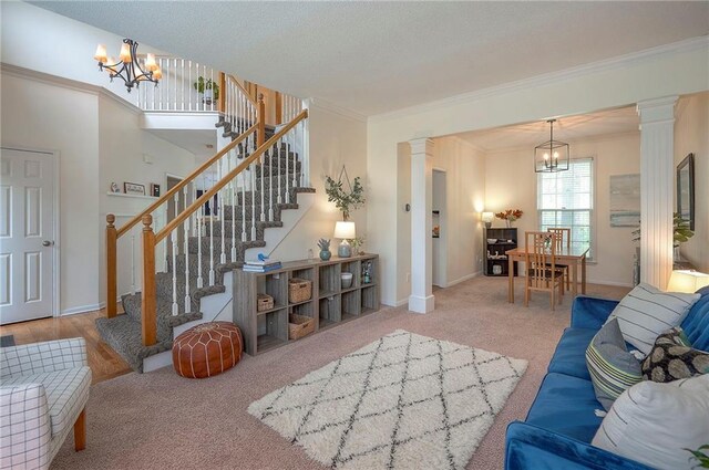 carpeted living room featuring an inviting chandelier, ornamental molding, decorative columns, and stairway