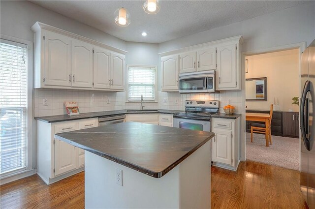 kitchen featuring dark countertops, wood finished floors, a sink, white cabinets, and stainless steel appliances
