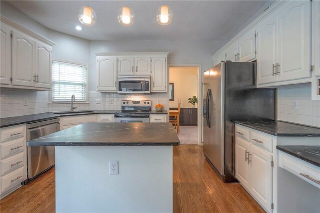 kitchen with white cabinets, dark countertops, a sink, stainless steel appliances, and tasteful backsplash