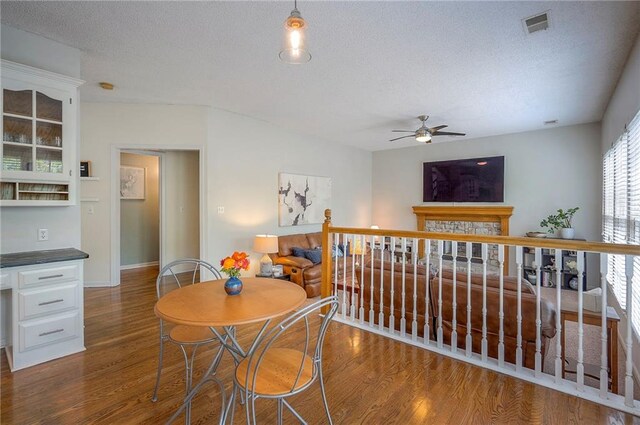 dining space featuring ceiling fan, a textured ceiling, baseboards, wood finished floors, and visible vents