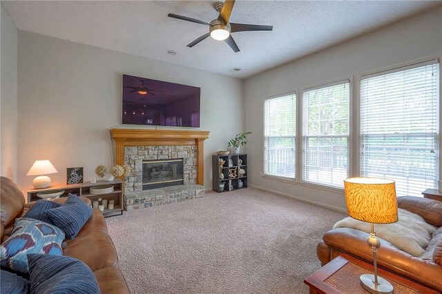 living area featuring carpet flooring, a textured ceiling, a stone fireplace, a ceiling fan, and baseboards