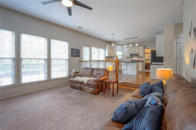 living room with baseboards, a textured ceiling, ceiling fan, and light colored carpet