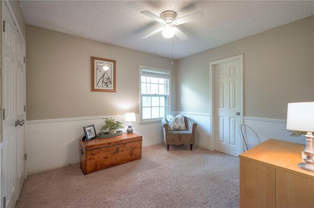 carpeted home office featuring a ceiling fan, a textured ceiling, and a wainscoted wall