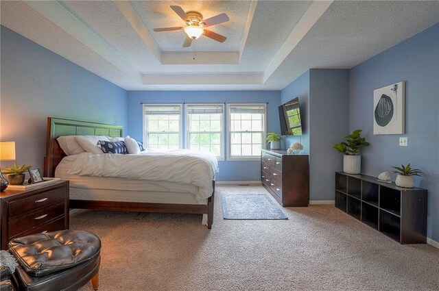 bedroom featuring baseboards, light colored carpet, a textured ceiling, a tray ceiling, and a ceiling fan