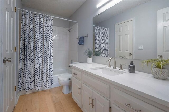bathroom featuring toilet, wood finished floors, shower / tub combo with curtain, and vanity