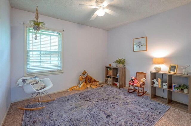 playroom featuring a ceiling fan, baseboards, carpet, and a textured ceiling