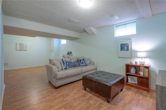 living room featuring light wood-style floors, a textured ceiling, baseboards, and visible vents