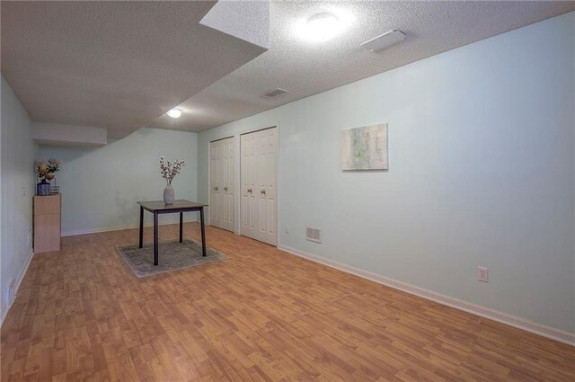 interior space with baseboards, light wood finished floors, a textured ceiling, and visible vents