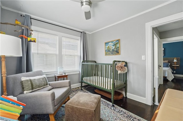 bedroom with baseboards, ornamental molding, a crib, and wood finished floors