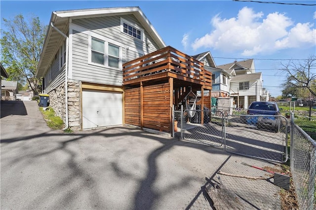view of front of house with driveway, a deck, a gate, fence, and stone siding