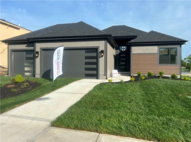 prairie-style house featuring an attached garage, roof with shingles, and a front yard