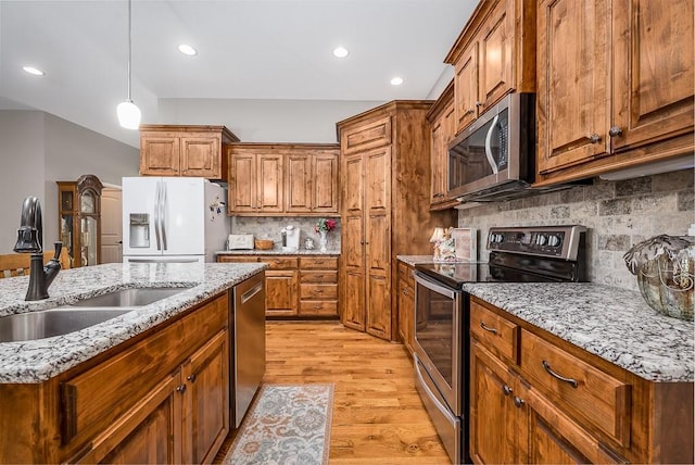 kitchen with brown cabinetry, backsplash, a sink, light wood finished floors, and stainless steel appliances