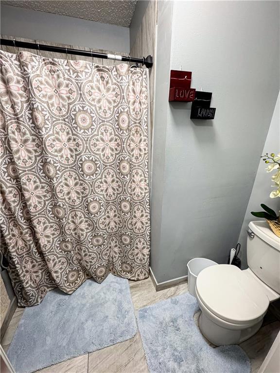4024 NE 59th Ter, Gladstone, MO 64119 - full bathroom featuring toilet, a shower with curtain, baseboards, and a textured ceiling