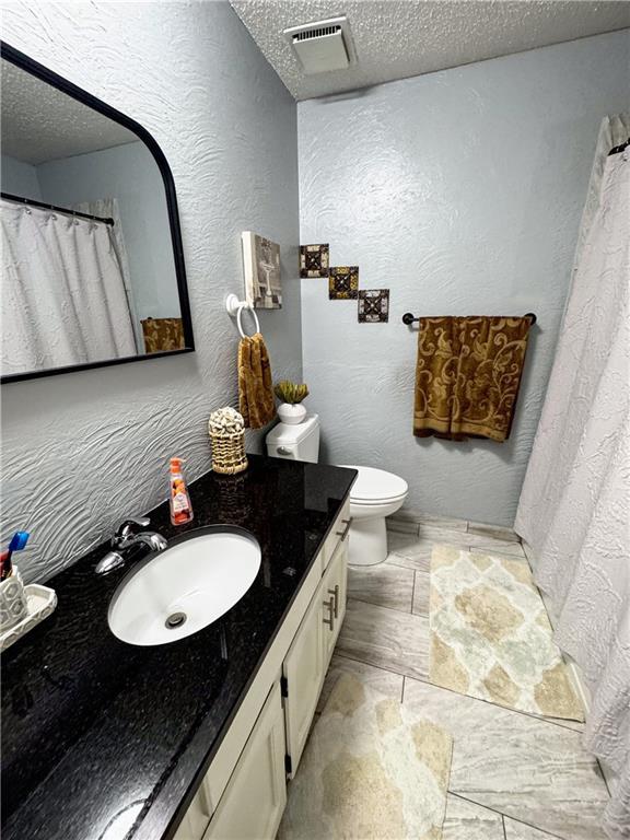 4024 NE 59th Ter, Gladstone, MO 64119 - full bathroom with a textured ceiling, visible vents, vanity, toilet, and a textured wall