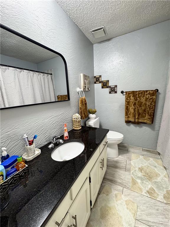 4024 NE 59th Ter, Gladstone, MO 64119 - bathroom featuring a textured ceiling, visible vents, vanity, toilet, and a textured wall