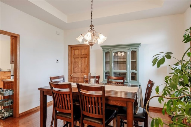 dining area featuring baseboards, an inviting chandelier, wood finished floors, and a raised ceiling
