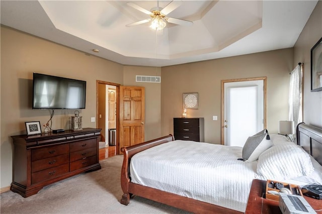 bedroom featuring visible vents, ceiling fan, a tray ceiling, and light carpet