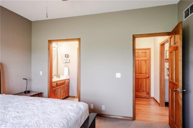 bedroom featuring baseboards, light wood finished floors, ensuite bath, and visible vents