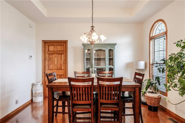 dining area with visible vents, a raised ceiling, baseboards, a notable chandelier, and hardwood / wood-style floors