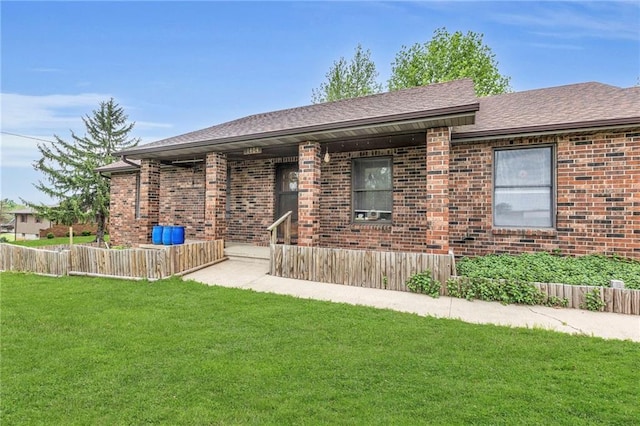 view of front of property with roof with shingles, fence, brick siding, and a front yard