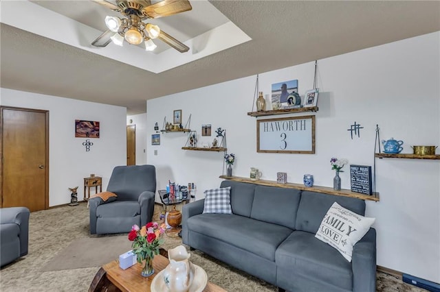 carpeted living area featuring a raised ceiling, ceiling fan, and a textured ceiling