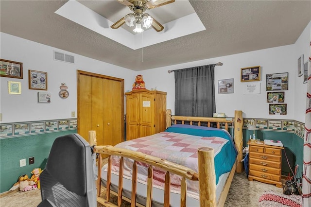 bedroom with a tray ceiling, a ceiling fan, a textured ceiling, and visible vents