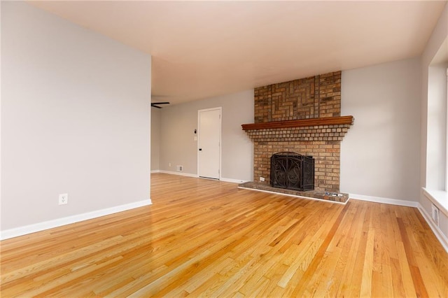 unfurnished living room with baseboards, a brick fireplace, and wood finished floors