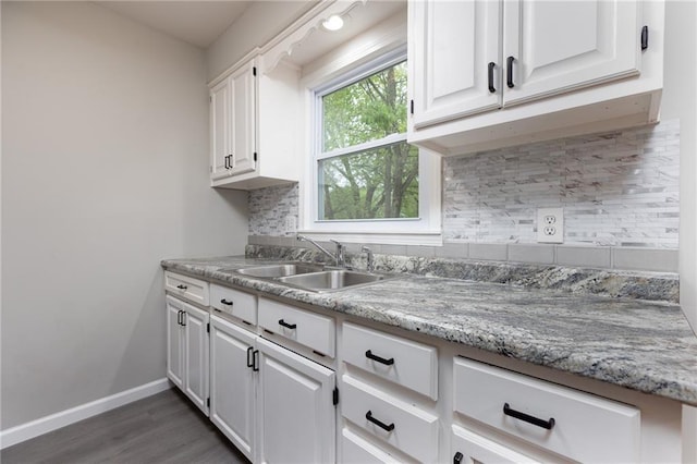 kitchen featuring tasteful backsplash, wood finished floors, a sink, baseboards, and white cabinetry