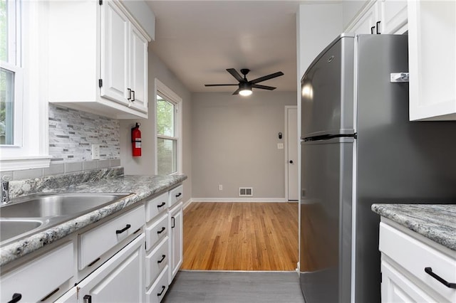 kitchen featuring ceiling fan, tasteful backsplash, freestanding refrigerator, light wood-style floors, and white cabinetry