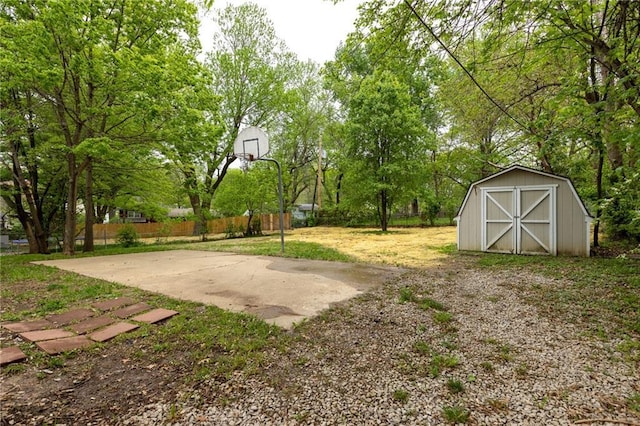 view of yard with basketball court, fence, an outdoor structure, and a storage unit