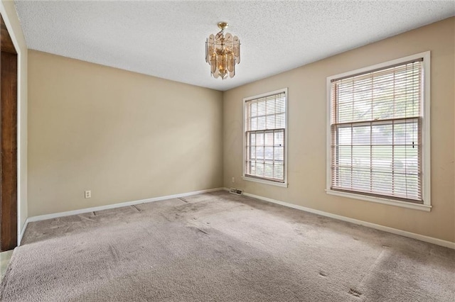 carpeted spare room featuring baseboards, a textured ceiling, and a notable chandelier
