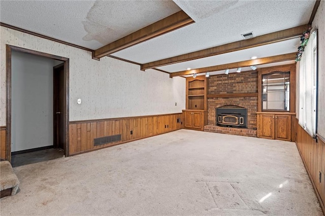 unfurnished living room featuring visible vents, wood walls, a textured ceiling, and a wainscoted wall