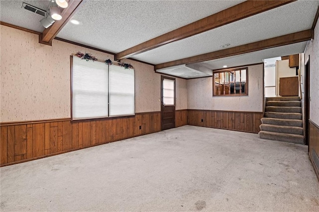 interior space featuring a textured ceiling, wainscoting, beam ceiling, wooden walls, and carpet