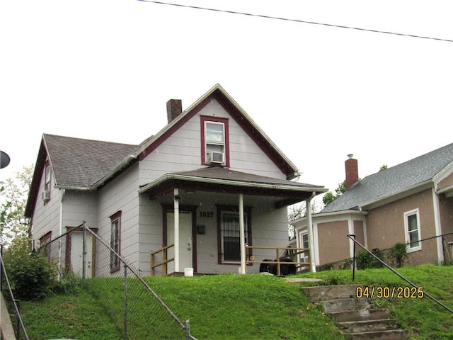 bungalow-style house with fence, covered porch, a front yard, a chimney, and a shingled roof