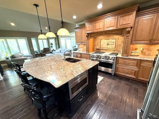 kitchen with light stone countertops, a sink, a breakfast bar area, stainless steel appliances, and open floor plan