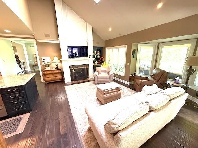 living area with dark wood-style flooring, a fireplace with flush hearth, high vaulted ceiling, baseboards, and recessed lighting