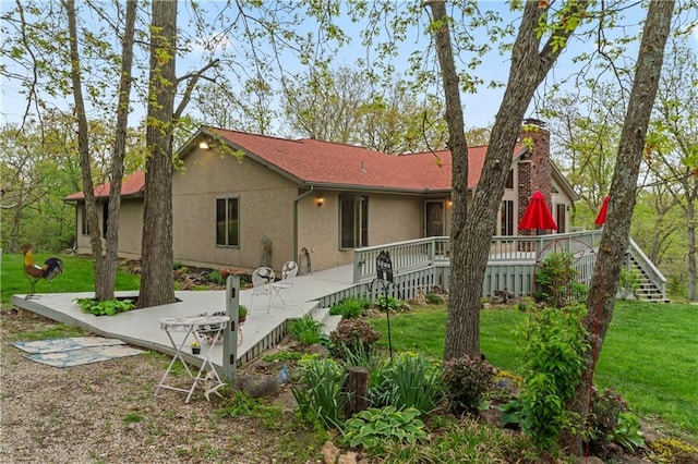 rear view of house featuring a wooden deck, stucco siding, a chimney, a yard, and stairway