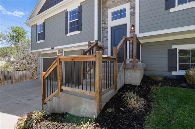 view of exterior entry with a garage, fence, and driveway