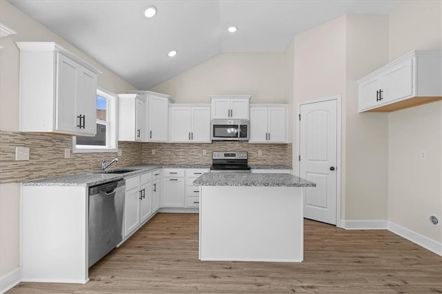 kitchen featuring backsplash, appliances with stainless steel finishes, a center island, vaulted ceiling, and white cabinetry