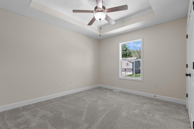 carpeted spare room with a raised ceiling, ornamental molding, baseboards, and a ceiling fan