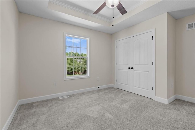 unfurnished bedroom featuring carpet floors, a tray ceiling, visible vents, and ornamental molding