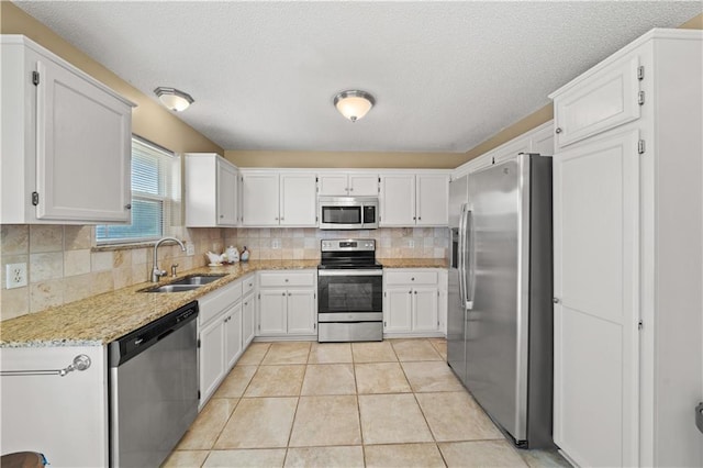 kitchen featuring light stone countertops, white cabinets, tasteful backsplash, a sink, and stainless steel appliances