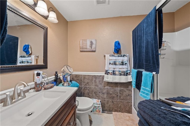 bathroom featuring visible vents, vanity, wainscoting, tile walls, and a shower stall
