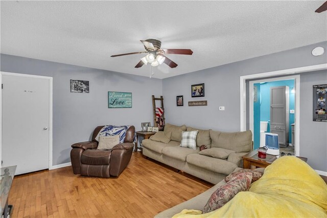 living room featuring baseboards, a ceiling fan, a textured ceiling, and wood finished floors