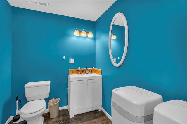 half bathroom with toilet, baseboards, visible vents, and wood finished floors