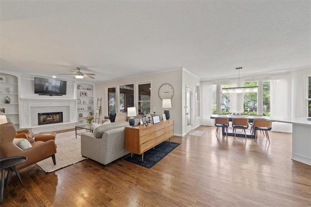 living area featuring built in features, wood finished floors, a fireplace, baseboards, and ceiling fan